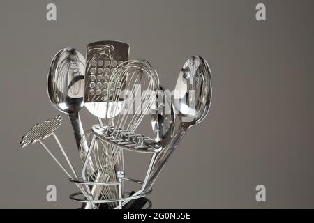 Stainless steel chrome spatular, masher, spoons and whisk in kitchen tools utensil container. Stock Photo