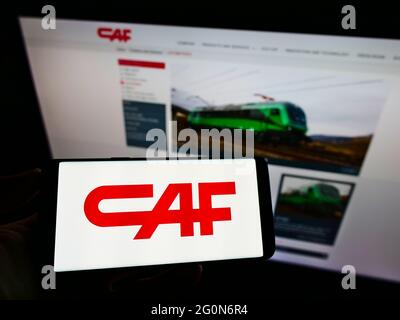 Person holding mobile phone with logo of Construcciones y Auxiliar de Ferrocarriles S.A. (CAF) on screen in front of webpage. Focus on phone display. Stock Photo
