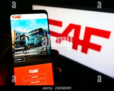 Person holding mobile phone with website of Construcciones y Auxiliar de Ferrocarriles (CAF) on screen with logo. Focus on center of phone display. Stock Photo