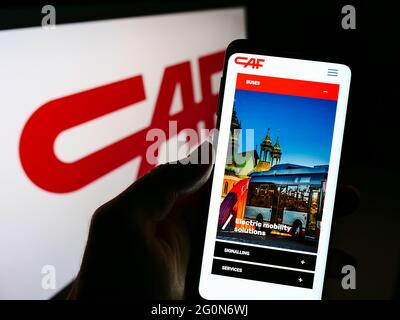 Person holding cellphone with webpage of Construcciones y Auxiliar de Ferrocarriles (CAF) on screen with logo. Focus on center of phone display. Stock Photo