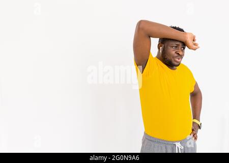 Tired afro american guy feeling tired after difficult online workout exercising in headphones wearing yellow t-shirt. Sport beginner exhausted working Stock Photo