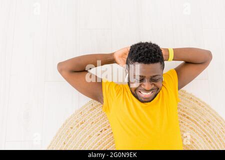 Sporty African American male doing home training and exercising doing sit-ups abs exercises crunches in headphones Indoors. Young active man smiling Stock Photo