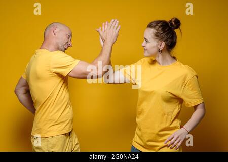 Smiling man and the woman in the yellow clothes give a high five. Bright background. Stock Photo