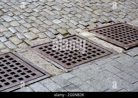 drainage system of urban infrastructure with an iron grating of the hatch of the stormwater system of the sidewalk from granite tiles near the road fr Stock Photo