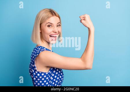 Profile side photo of young cheerful girl happy positive smile show hands muscles biceps strong isolated over blue color background Stock Photo