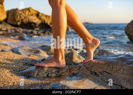 Woman on rock at beach dipping toes in water, having fun outdoor lifestyle in Matosinhos, Portugal Stock Photo