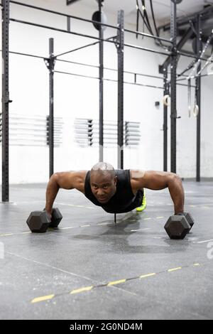 African American man doing pushups with kettlebells on gym floor. Intense workout of body strength. Stock Photo