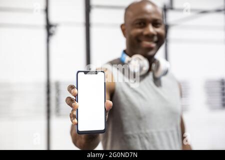 Black sportsman smiling showing the blank screen of a smartphone. Concept of sports apps. Selective focus.
