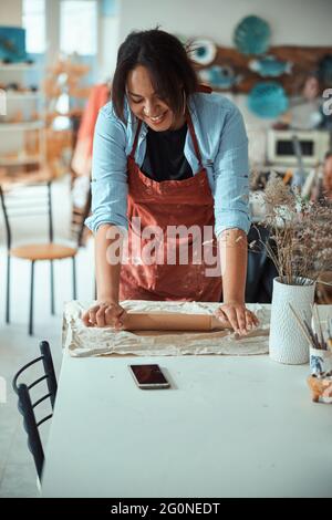 Smiling craftswoman in apron working in pottery workshop Stock Photo