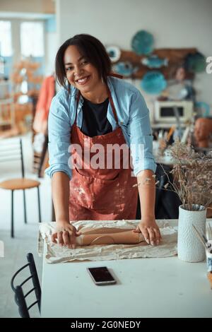 Joyful craftswoman in apron working in pottery workshop Stock Photo