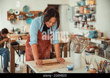 Cheerful craftswoman in apron working in pottery workshop Stock Photo