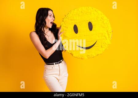 Photo of young woman amazed shocked surprised look hold paper pinata emoji smile isolated over yellow color background Stock Photo