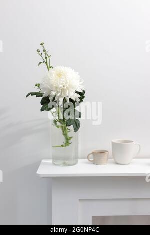 A large chrysanthemum in a glass vase, two fluted cups of coffee and ceramic bird figurines on the table. Office decoration. Copy space Stock Photo