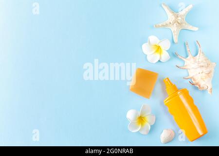 Summer sunscreen, seashells, starfish and frangipani tropical flowers on blue background top view Stock Photo