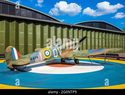 Imperial War Museum IWM Duxford - replica Spitfire static display on RAF roundel base outside a vintage aircraft hangar. Stock Photo