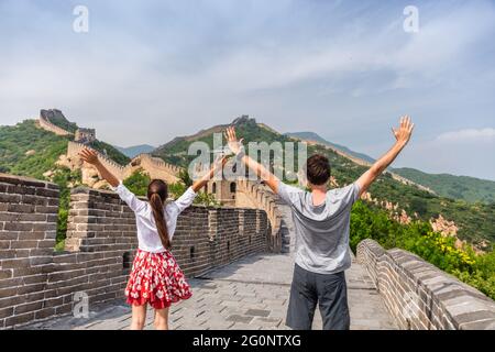 China travel at Great Wall. Tourists couple happy cheering in Asia on famous Chinese tourist attraction in Beijing. Young people with arms up in Stock Photo