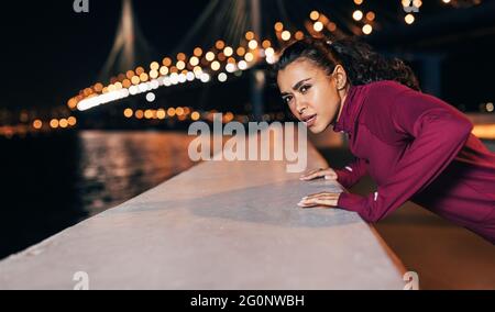 Young mixed race female athlete doing push-ups on an embankment at evening Stock Photo