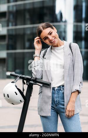 Smiling woman standing outdoors with electric scooter looking at camera Stock Photo