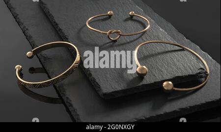 Three modern design gold bracelets on natural black stone plates Stock Photo