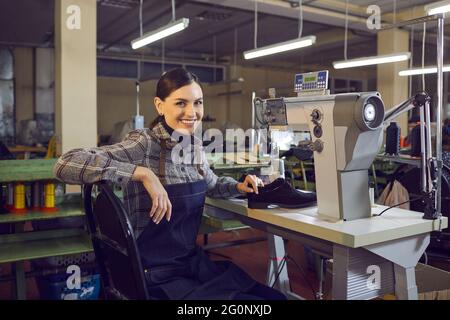Smiling female shoemaker sitting at workplace looking at camera portrait Stock Photo