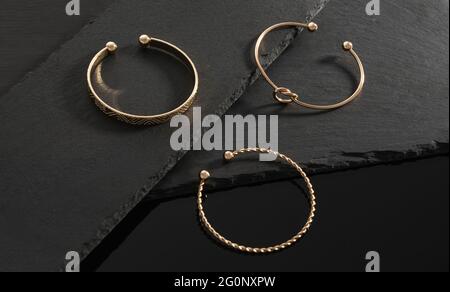 Three modern design golden bracelets on black stone plates on black background Stock Photo