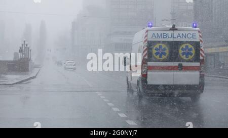 Ambulance with flashing lights moves down the street in bad weather. Stock Photo