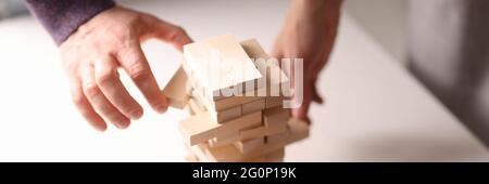Several hands reach for wooden blocks from the toy tower Stock Photo