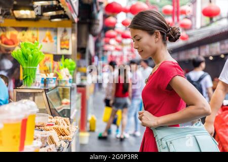 Woman tourist at chinese market Wangfujing, food street on Asia travel. Traditional Beijing snacks at outdoor market place. Asian woman looking at Stock Photo