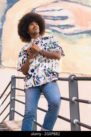 young black guy with afro hair standing leaning on a metal railing Stock Photo