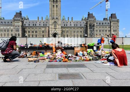 Ottawa, Canada - June 2, 2021: People gather round and leave shoes and toys left near the Centennial Flame on Parliament Hill in memory of the 215 children whose remains were found near of former Residential School in Kamloops, B.C. Equipment for a smudging ceremony is visible. Stock Photo
