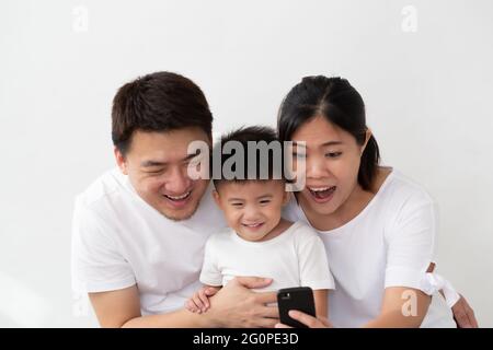 Cheerful young Asian family with son making selfie and smiling with mobile phone on front camera isolated on white background Stock Photo