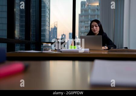 Business woman tired office worker sitting at desk using computer and doing overtime project in the workplace Stock Photo