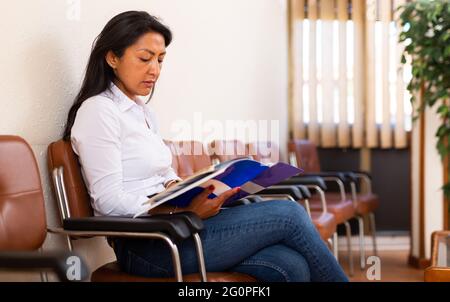 Focused Hispanic female entrepreneur reading documents in office hall Stock Photo