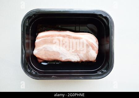 Pork belly cut stored in black plastic box against white background Stock Photo