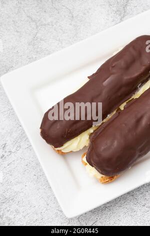 Chocolate eclair with a custard cream filling on a white plate.  With a concrete background Stock Photo