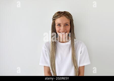 Cheerful attractive female with braids wearing casual white shirt standing on light background and looking at camera Stock Photo