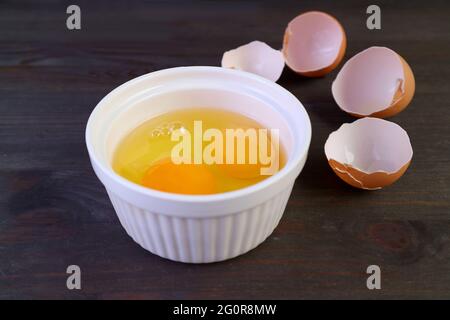 Vibrant color raw eggs in a bowl with cracked eggshells in the backdrop Stock Photo