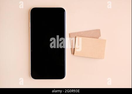 Mobile phone mockup with blank screen and business cards isolated on beige paper. Business card made of craft paper and smart phone. High quality photo Stock Photo
