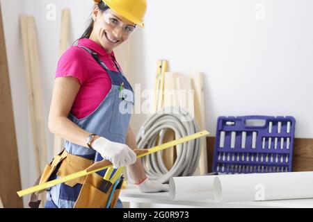 Woman builder in protective helmet and overalls holding ruler in her hands Stock Photo