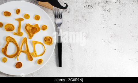Celebrating Father's Day. Breakfast: pancakes in form of congratulations - I love dad , and coffee mug and copy space. Stock Photo