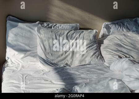 Unmade messy bed with white bedsheet Stock Photo