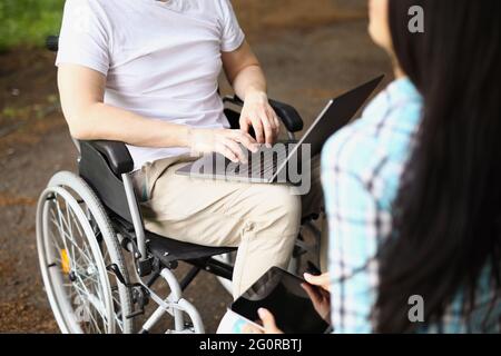 Man in wheelchair works on laptop on street next to woman sits and holds tablet Stock Photo