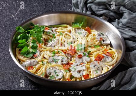Italian pasta with cremini mushroom sauce of heavy cream and parmesan  cheese with crispy bacon and fresh parsley served on a metal skillet on a dark