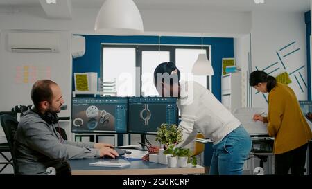 Multiethnic team sharing ideas about industrial project using two monitors with 3D gears and metalic clamp using CAD software. Industrial engineer and black manager innovating prototype of motor Stock Photo