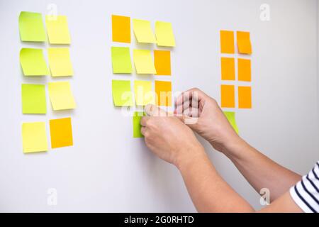 IT worker tracking his tasks on kanban board. Using task control of agile development methodology. Man attaching sticky note to scrum task board in th Stock Photo