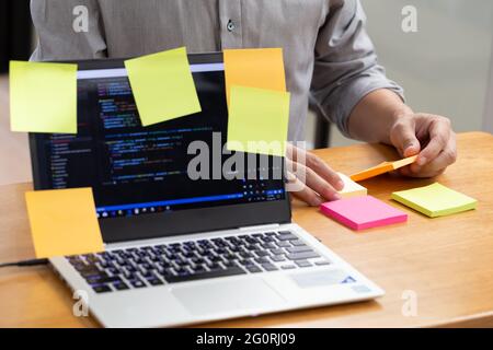 Tasks on sticky note cards on laptop computer with source code program of business software development planning and programmer holding short note pap Stock Photo