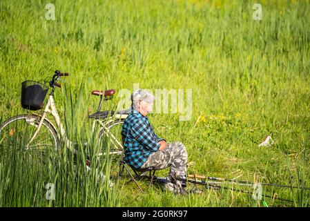 Skierniewice, Poland - May 31, 2021: Angler with fishing rods and a bicycle on a background of green grass in the rays of the sun. Stock Photo