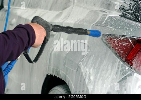 Man washing a car with a brush spreading shampoo over it. A scene from self service car wash. Stock Photo