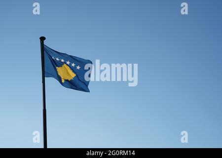 Kosovo flag hoisted on a flagpole waving in the wind. Low angle view against blue sky with plenty of copy space. Stock Photo