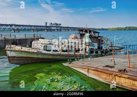 Semi-flooded river pleasure vessel at an abandoned pier on background of railway bridge Stock Photo